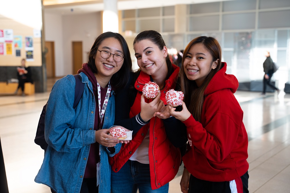 three students holding doughnuts